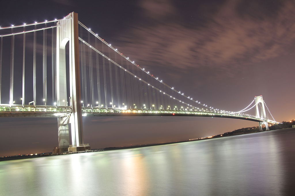 Foto del Puente Verrazano-Narrows de noche visto desde Brooklyn de Violinbd / CC BY-SA (https://creativecommons.org/licenses/by-sa/3.0), vía Wikimedia disponible en https://commons.wikimedia.org/wiki/File:Verrazano-Narrows_Bridge_@_Night_from_Brooklyn.JPG