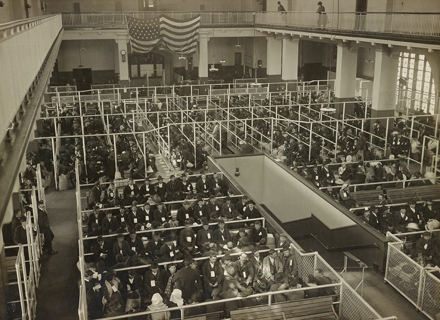 Imagen histórica en blanco y negro de inmigrantes esperando en el Gran Salón de Ellis Island para el control de ingreso de la aduana de Nueva York. Foto de  The New York Public Library en Unsplash disponible en https://unsplash.com/photos/zVFLhNlNj7g