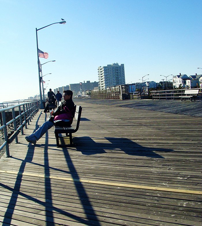 Personas mirando el mar desde las bancas en el boardwalk de Rockaway Beach en Queens - Foto de AHM