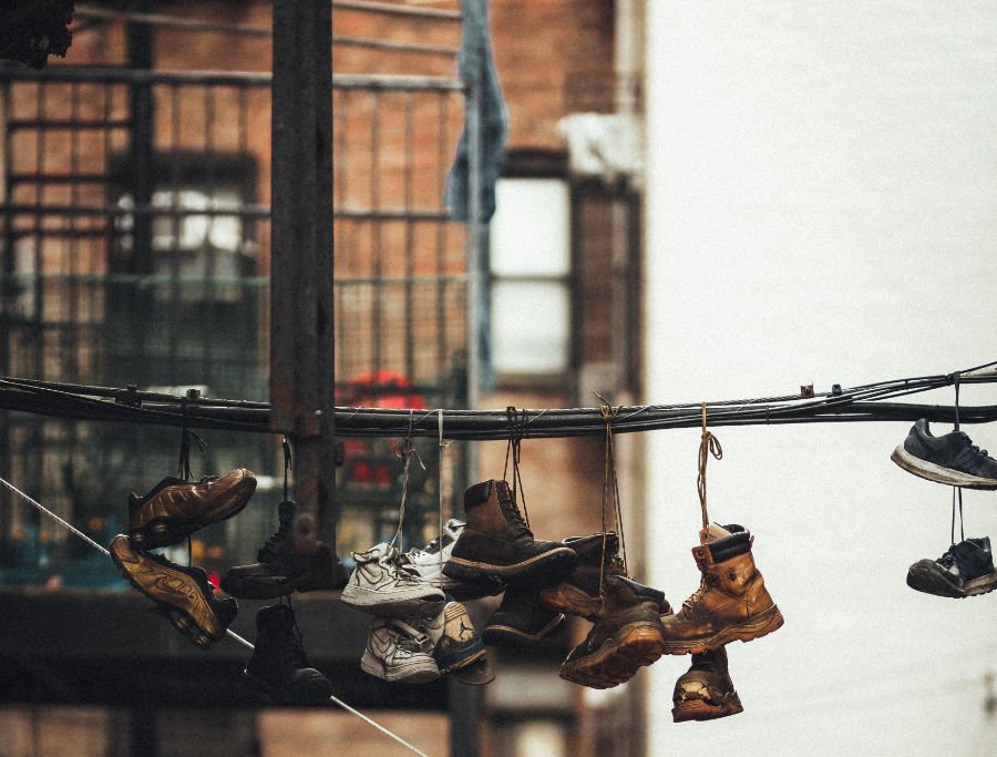 Zapatos colgando en un cable, al fondo los típicos edificios de Bed-Stuy en Brooklyn. Foto de Lerone Pieters en Unsplash, con Licencia Unsplash, disponible en https://unsplash.com/photos/DLrRvTcmadY