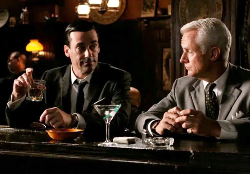 Don Draper y Roger Sterling bebiendo un la barra de un bar de Manhattan - Captura de la pantalla de la serie de HBO. Lista de Bares de Mad Men que aún funcionan.